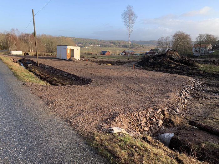 Nyplanerat område med grus och material utlagt längs en väg under byggarbete.