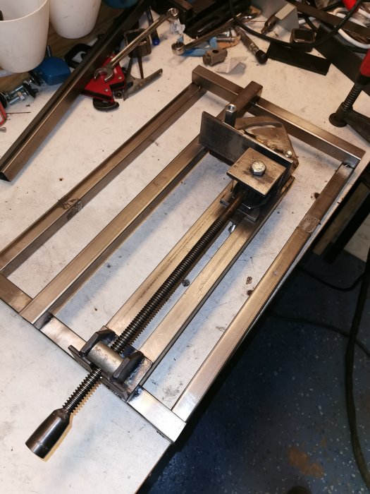 Hemmagjord metallkonstruktion med 25x25-fyrkantsrör och en trapetsgängad stång på ett arbetsbord.