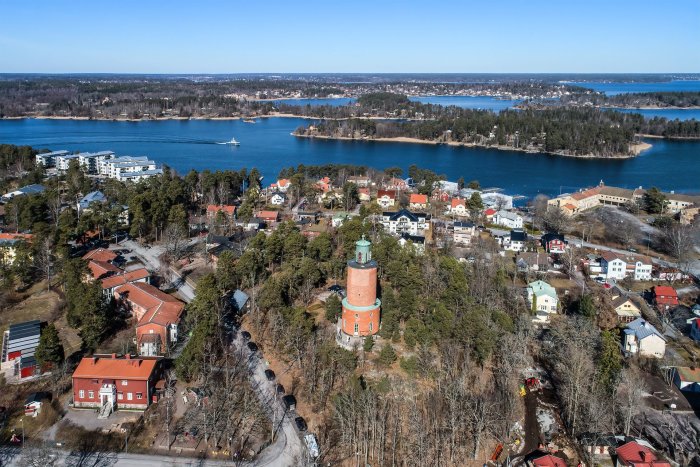 Flygbild över Vaxholm med historiskt torn och omgivande bostäder mot havsutsikt.