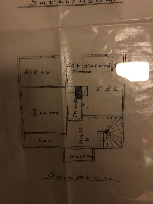 Grundritning av en övervåning med markerade rum som kök och hall, samt en spiraltrappa och en balkong.