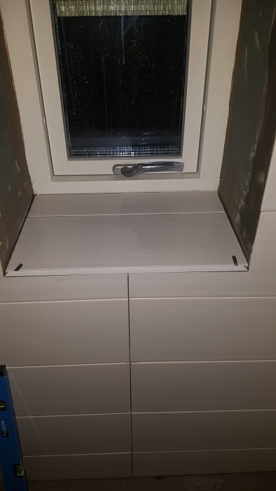 Nyinstallerad, vitmålad fönsterbräda under ett stängt fönster med nyligen målade paneler nedanför.