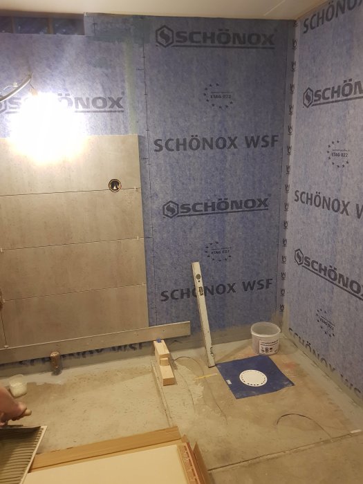 Renoveringsarbetet i badrum med väggar täckta av Schönox isolermaterial och några kakelplattor installerade.