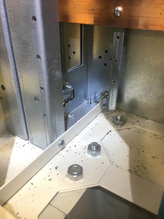 Stålkonstruktion med skruvar och spån samlade på bottenplattan i en elcentral, visande potentiell slarvig installation.