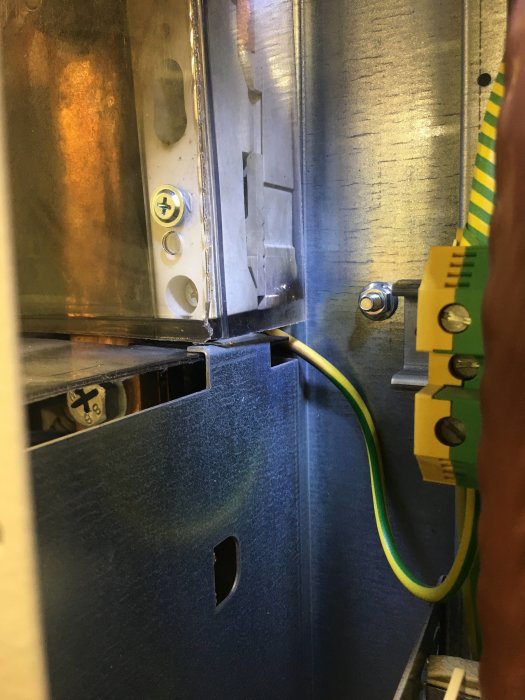 Inre del av elcentral med elektrisk anslutning nära jordningsskena och synliga skruvar.