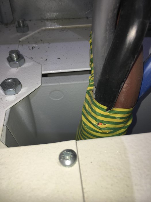 Elledningar med isoleringsskador nära en skruv och metallyta inuti en elektrisk installation.