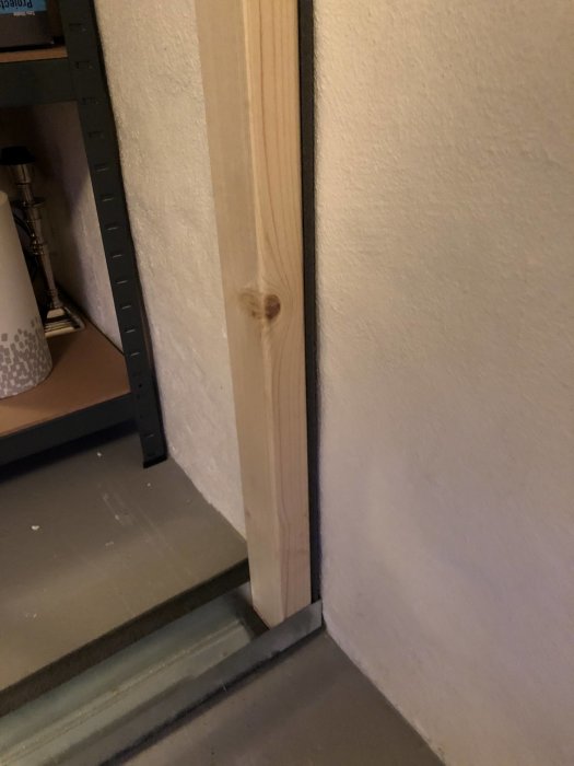 Träregel står vertikalt i hörn av källarvägg utan gips, intill putsad yta.