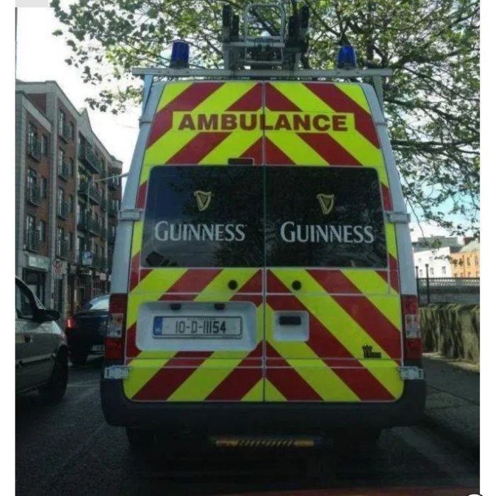 Ambulans med reflextejp och Guinness-loggor på bakdörrarna parkerad på gata.