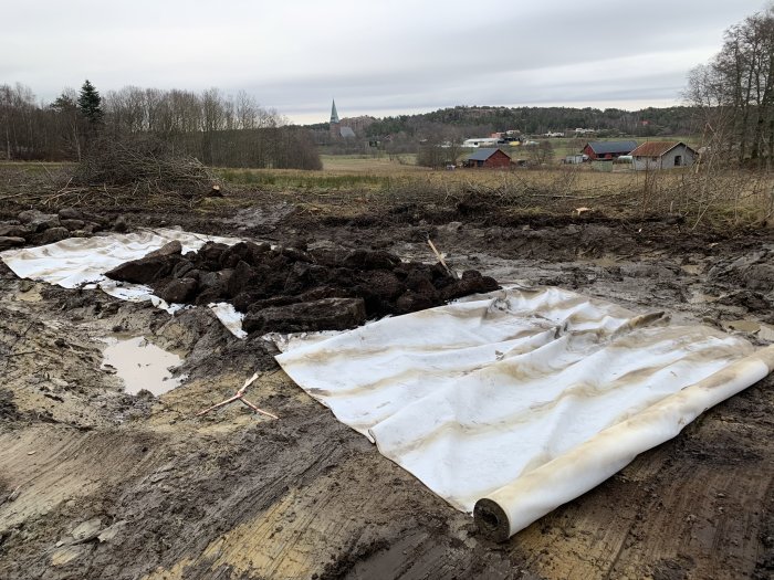 Vägbygge med ett rör på marken, geotextilduk och uppriven jord, i landsbygdsområde.