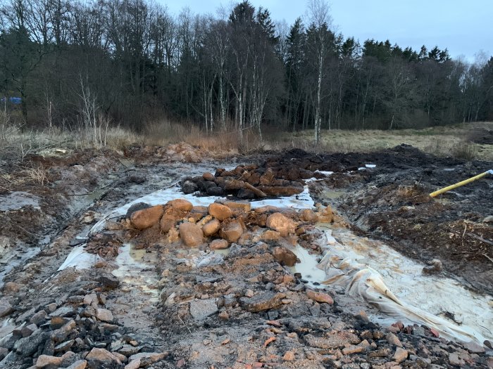 En grävd vägbyggnadsplats med lera, stenar och ett gult elrör som förberedelse för framtida infrastruktur.