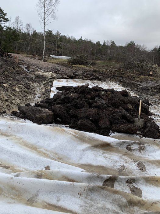 Grävd väg vid ett byggprojekt med synliga elrör, tomrör och snötäckt mark i ett skogsområde.