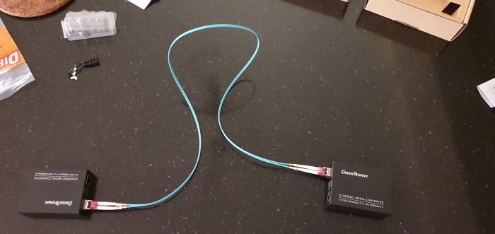 Multimode fiberkabel ansluten till två mediakonverterare på ett mörkt bord.