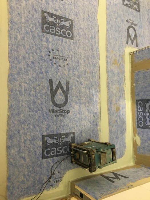 En bild på ett badrum under renovering med blått tätskikt på väggarna och en uppvikt hörna i förgrunden.