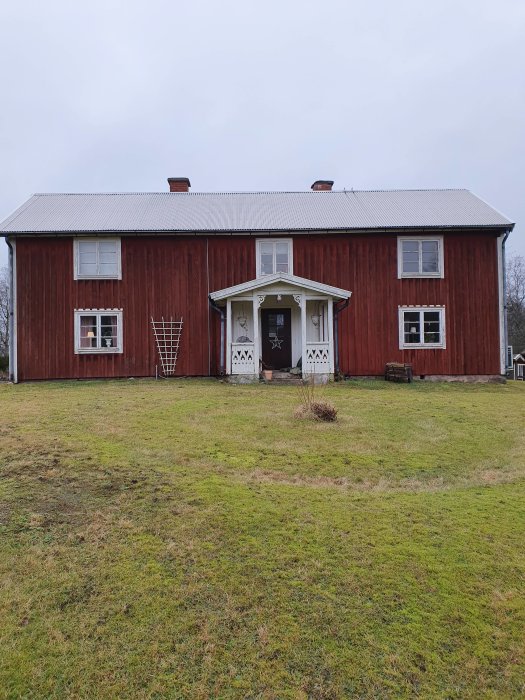 Rödmålat hus med vit sekelsskiftspanel och spröjsade fönster, gräsmatta i förgrunden.