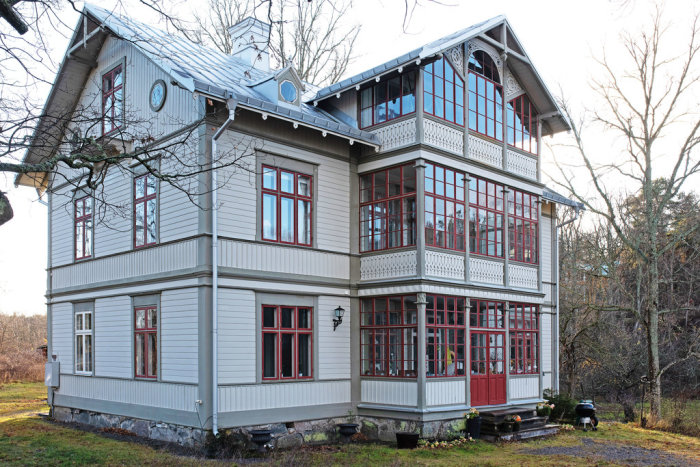 Tvåvåningshus i traditionell stil med vita och röda fönsterluckor och omgivande trädgård.