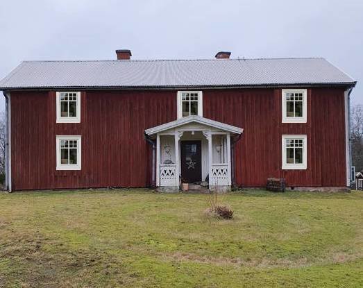 Traditionellt rött svenskt trähus med vita knutar och plåttak, omgivet av en gräsmatta.