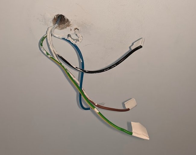 Fyra elektriska kablar sticker ut från ett hål i taket: blå, svart, brun och gul-grön.