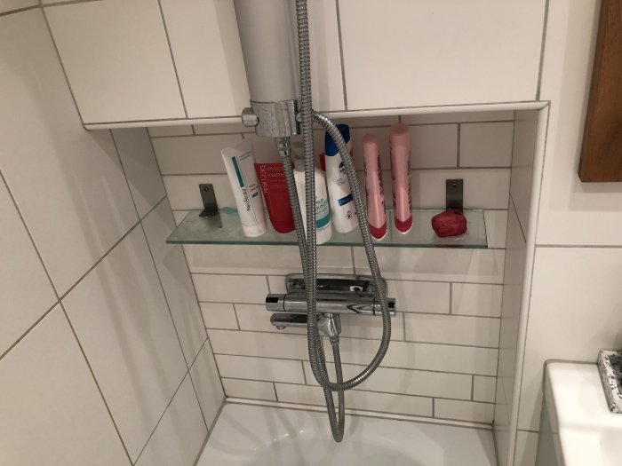 Infasad vit kaklad duschvägg med hylla, duschmunstycke och badrumsprodukter, storlek markerad för renovering.