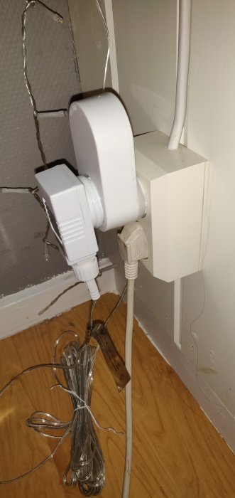 Vägguttag med insatt Trådfri smart plug och kontakt, intill ligger en upprullad ljusslinga.