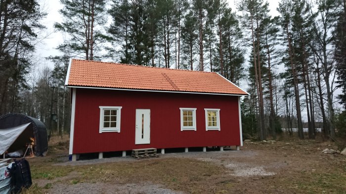 Nybyggt rödfärgat hus med vita fönsterfoder och dörr, omgivet av träd i ett vinterlandskap.