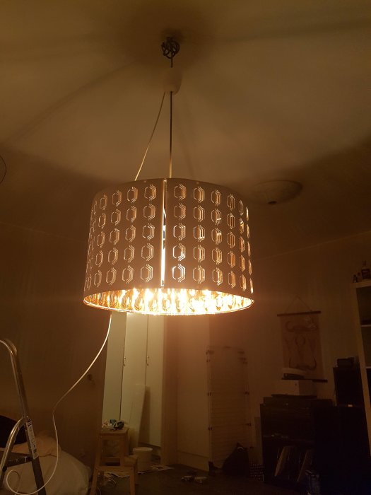 Hängande lampa med tänd ljus i rum under provisorisk installation med synliga kablar.