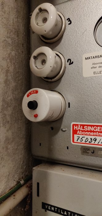 Elektriskt säkerhetsbrytare och keramiska isolatorer på en grå metallvägg.