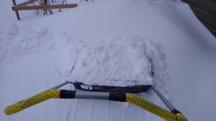 Snöskottning med snöräven belamrad med nysnö framför en snödriva.