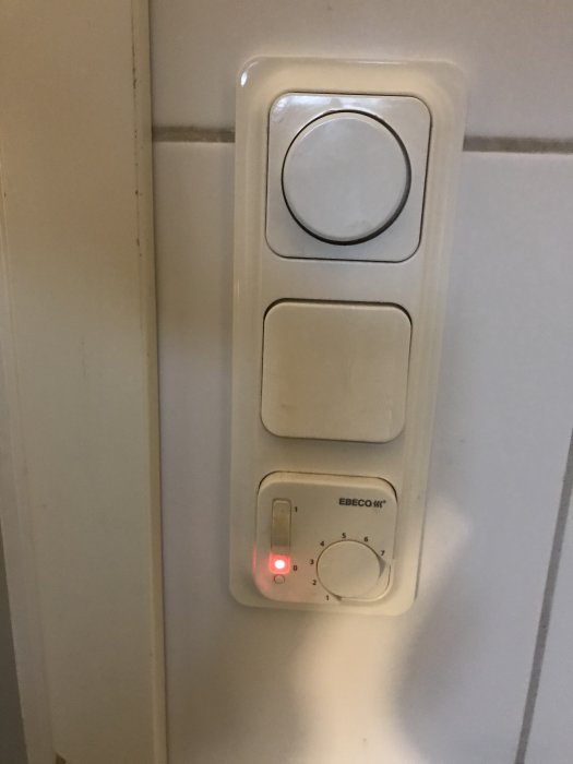 Strömbrytare med dimmer och golvvärmekontroll på en vägg, en röd indikatorlampa är tänd.