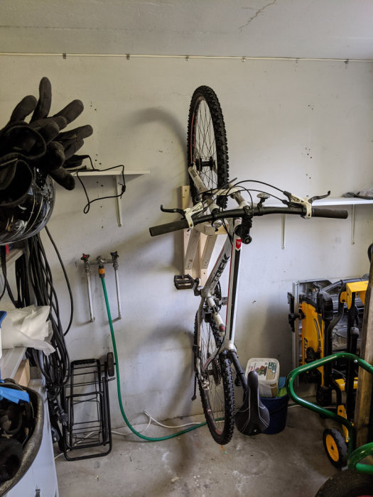 Organiserat garage med mountainbike upphängd på väggen, verktygslådor, och hylla för hjälmar och skor.