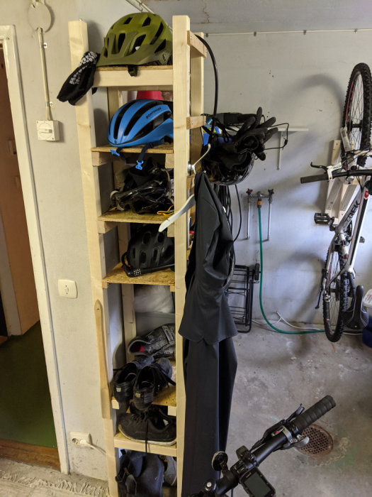 Organiserad garagehylla med hjälmar och skor, cykel på krok och arbetsyta i bakgrunden.