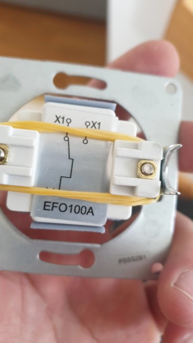 Närbild på en hand som håller en elektrisk installationskomponent med synlig märkning "EF0100A".