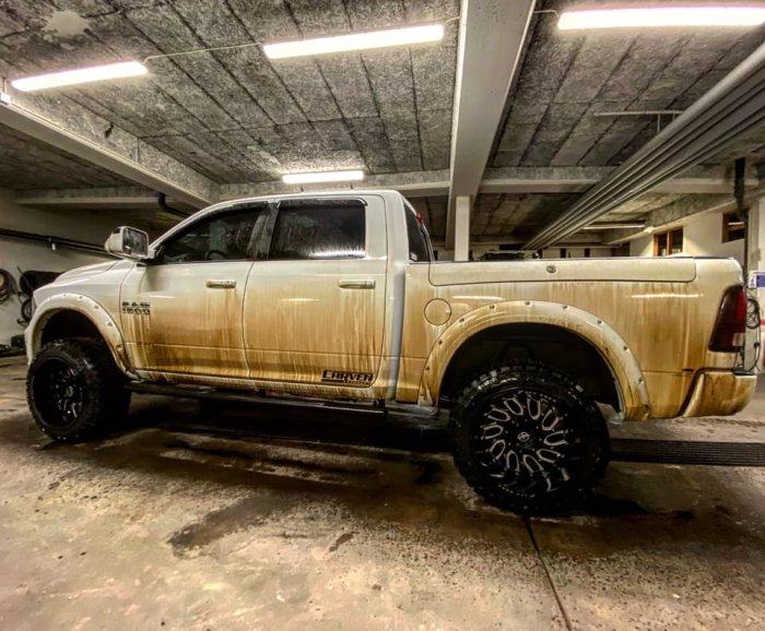 En pickup truck med kraftiga lerfläckar på sidorna parkerad i ett garage, illustrerar behovet av rengöring.