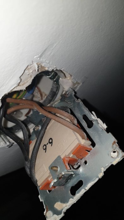Öppen elektrisk dosa med flera svarta ledningar och synliga anslutningar i en vägg.