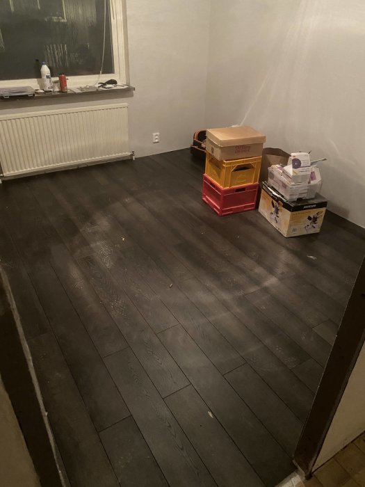 Nyrenoverat rum med mörkt Ikea Gräsmark golv, flyttlådor och renoveringsmaterial vid fönstret.