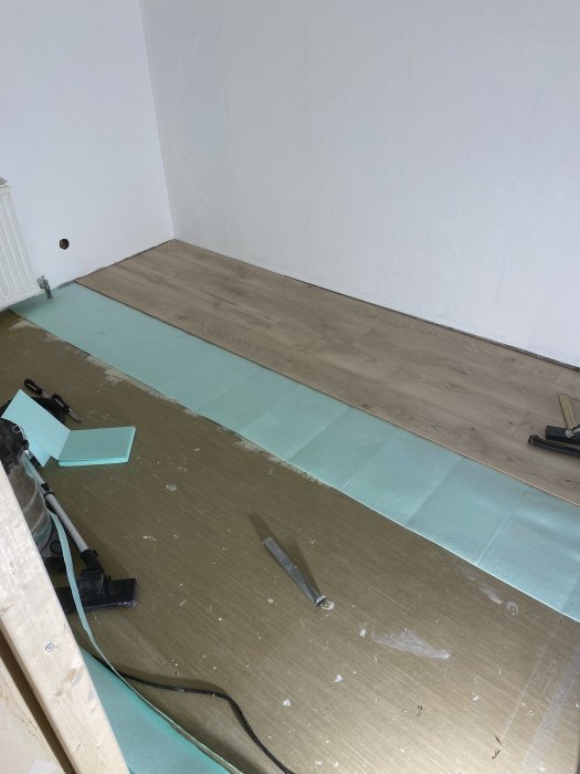 Pågående golvläggning av trälaminat med verktyg och skyddsplast i ett rum under renovering.