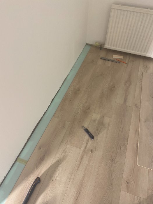 Pågående golvläggning med Ikeas Gräsmark golv, verktyg synliga nära en radiator och en omonterad planka.