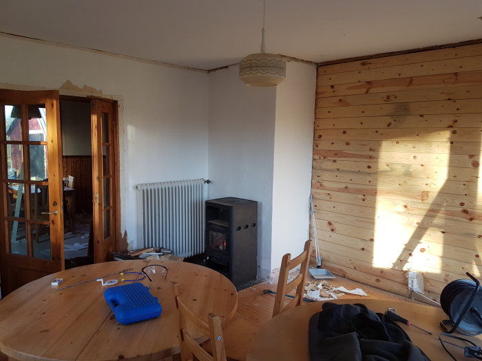 Vardagsrum före renovering med "hjärtväggen" klädd i spontade träbrädor, möbler och renoveringsmaterial.