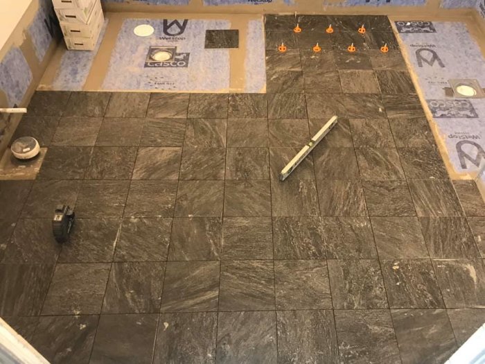 Halvlagt golv med mörka 25x25 cm plattor och Tebo Spin Level-system mellan vissa plattor.