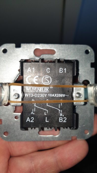 Närbild av en elektrisk kopplingsdosa hållen av en hand med synliga ledningar och märkningar.