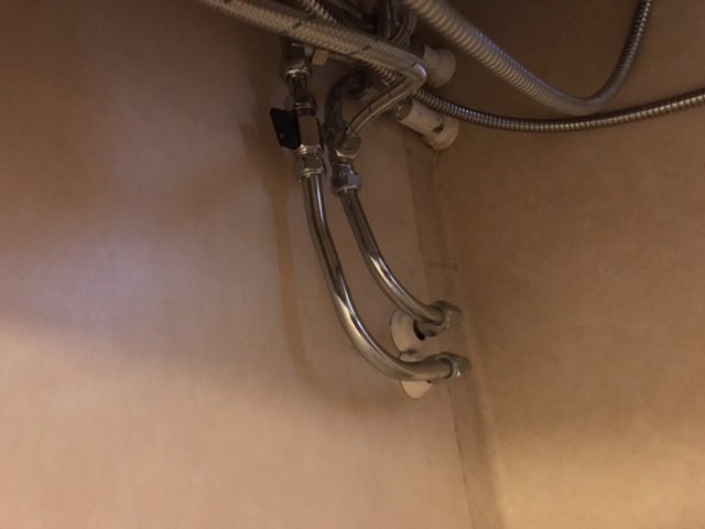 Röranslutningar och flexslangar under en värmekran, med begränsat utrymme för installation.