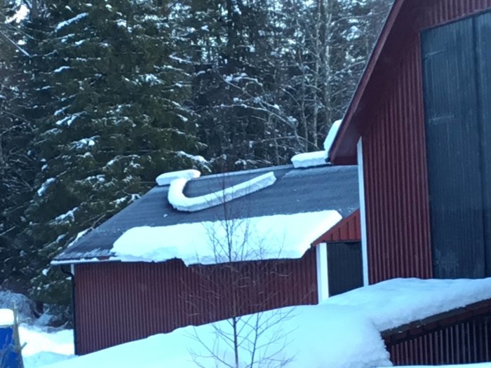 Snö formad som smileyansikte på ett rött garage med skog i bakgrunden.