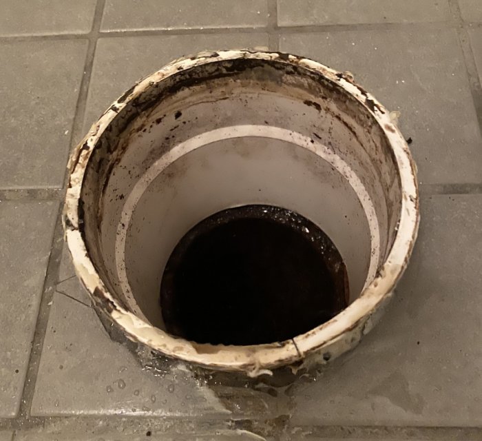 Öppen ände av ett skadat och smutsigt plastavloppsrör med mätt inner- och ytterdiameter.