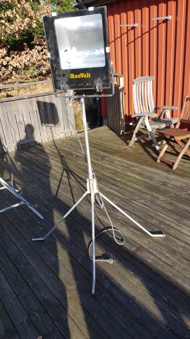 Högtrycksnatriumlampa med stativ på en trätrall framför en röd stuga och utemöbler.