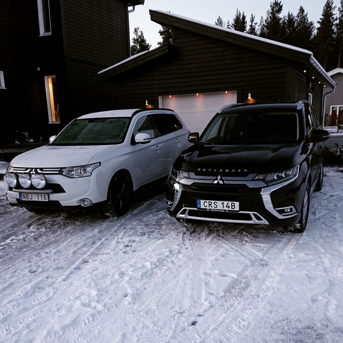 Två bilar parkerade framför ett hus med garage i vinterskymning, varav en är en laddhybrid.
