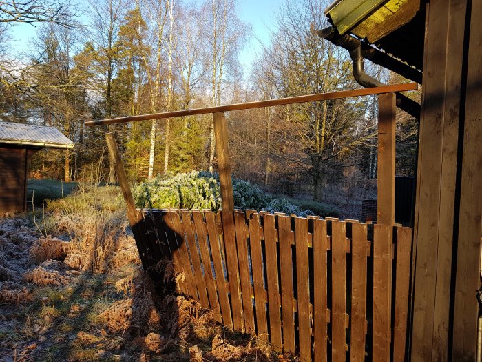 Trädäck med vikande trästaket och en överliggare mot en frostig, skogsbakgrund.