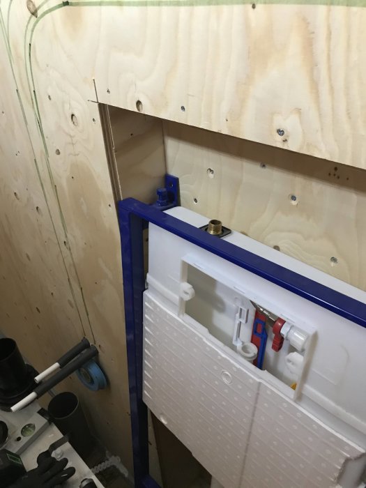 Konstruktionsfas av vägghängd toalett med plywoodvägg och installerad inbyggnadsstomme.