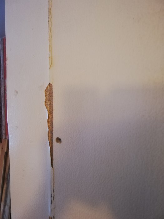 Skadad sektion av tunt, hårt puts lager på en vägg som är övermålad, hus från 1952.