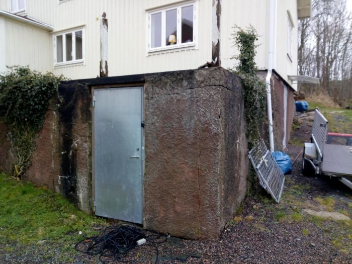 Utomhusvy av uppmurad uteplats med sliten ytterdörr och synlig skada på vägg.