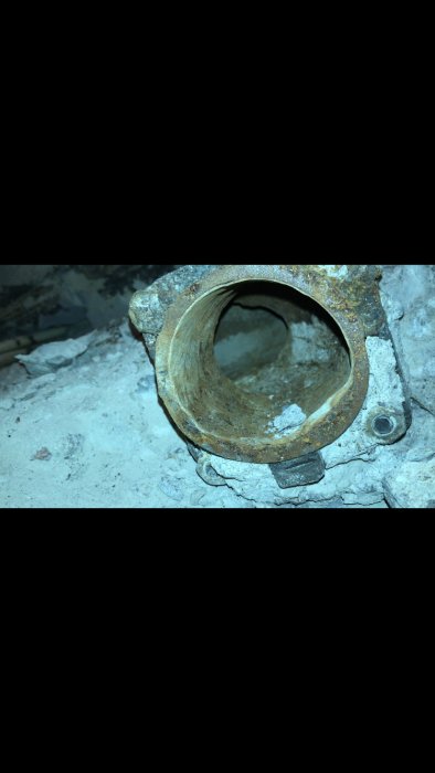 Äldre korroderat rör sedd inifrån med synliga avlagringar och rost, omgiven av sten och murbruk.