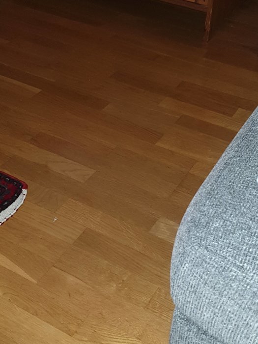 Träparkettgolv med fiskbensmönster, en del av en grå soffa och en hörna av en matta.