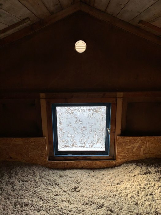 Insida av ett snedtak med exponerade takbjälkar och ett monterat fönster, fråga om bärande vägg.